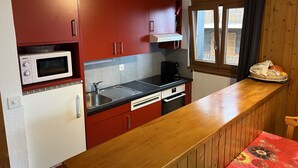 A compact kitchen with red cabinets, a microwave, a coffee maker, and a sink. - Mystical Apartment With Mountain Views (Veysonnaz)