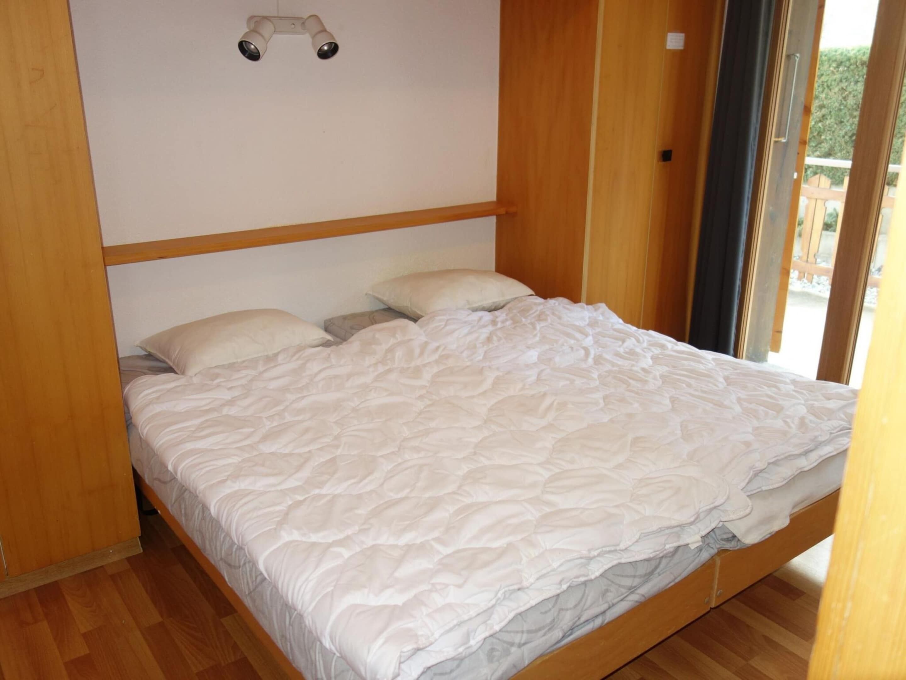 A single bed with a white duvet in a room with wooden flooring and a wooden headboard.