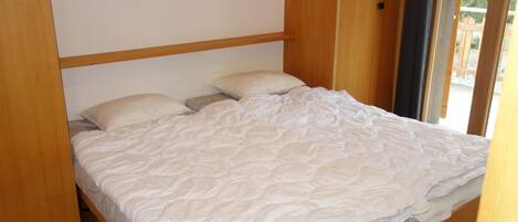 A single bed with a white duvet in a room with wooden flooring and a wooden headboard.