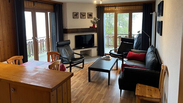 A cozy living room with a fireplace, a TV, a sofa, and a dining area. - Mystical Apartment With Mountain Views (Veysonnaz)