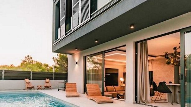 Uma casa moderna com piscina, área de estar externa e porta de vidro que dá para uma sala de estar.