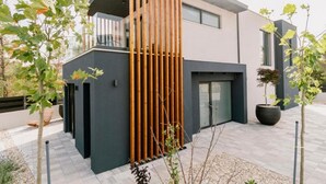 Um edifício moderno de dois andares com varanda, design em ripas verticais de madeira e um pátio pavimentado.