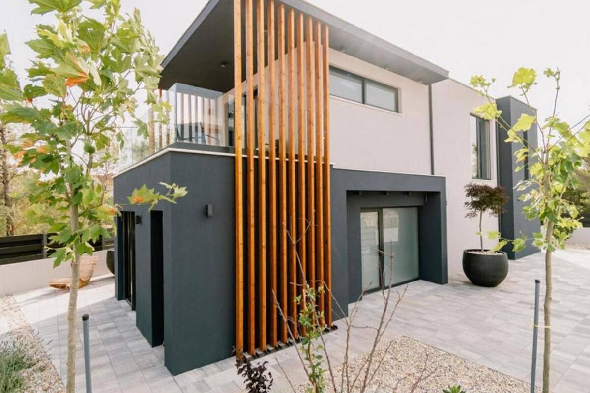 A modern two-story building with a balcony, a vertical wooden slat design, and a paved courtyard.