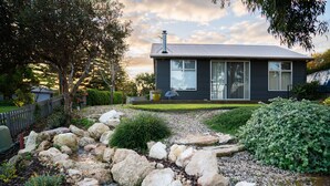 A modern house with a stone pathway leading to the entrance, surrounded by greenery and a fenced yard. - Pelican Cottage - Pet Friendly - Wifi (Goolwa North)