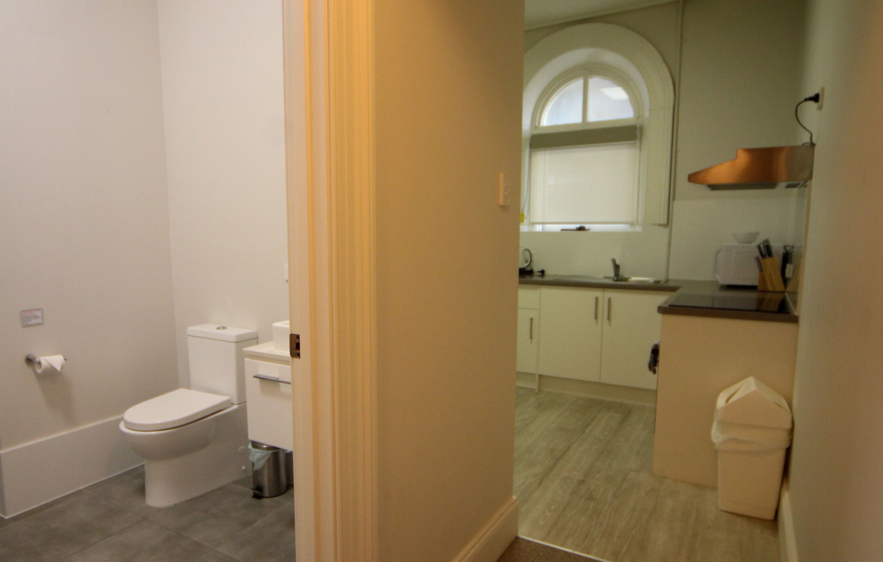 Ein Badezimmer mit Toilette und Mülleimer, eine Küche mit Spüle und Schränken sowie ein Fenster mit Blick ins Freie.