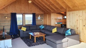 A log cabin interior with a sectional sofa, a small table, and a TV on a stand.