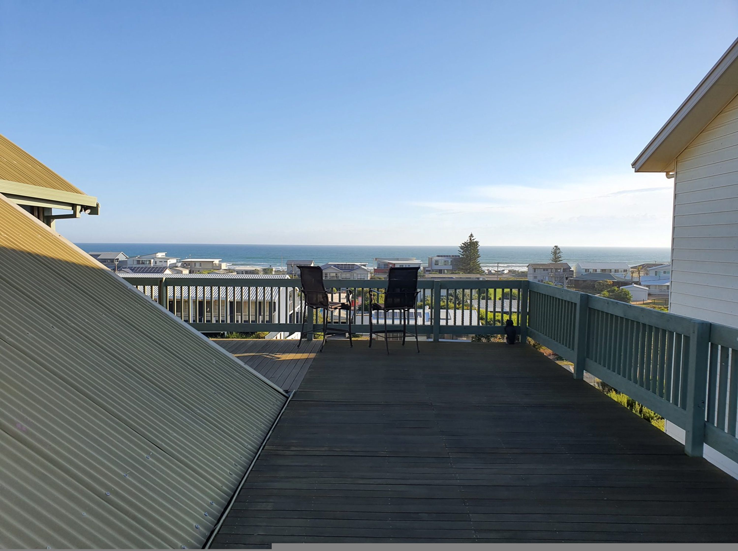 Una terraza de madera con dos sillas que da a la vista del mar.