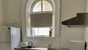 A kitchen with white cabinets, a built-in oven, a microwave, a sink, and a window with a view. - Seafield Tower Glenelg Apartment no 6 (Glenelg)