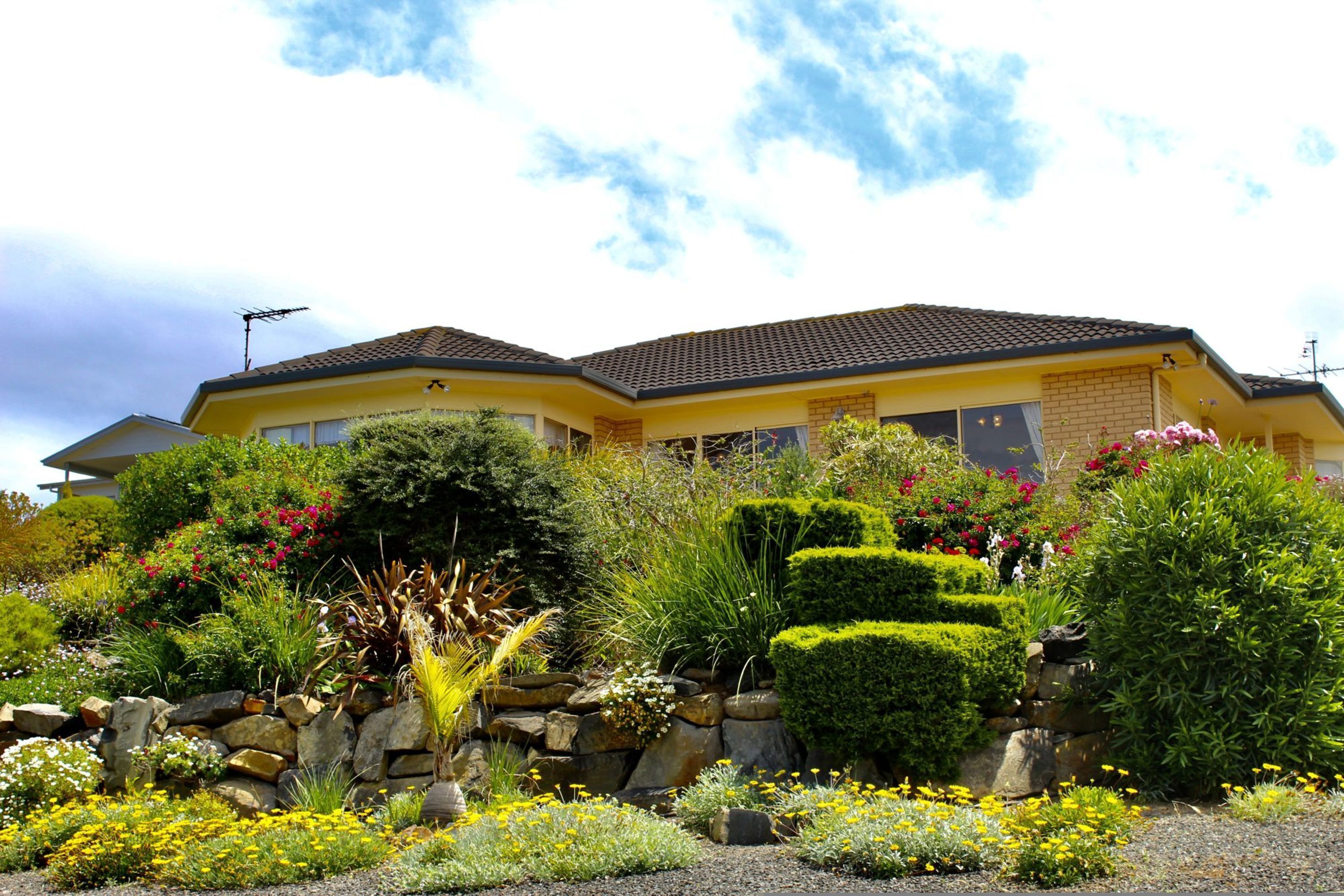 A two-story house with a tiled roof, surrounded by a well-maintained garden with various plants and flowers.