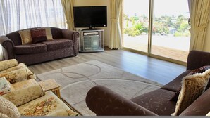 Una sala de estar con un sofá marrón, un televisor y un ventanal con cortinas.