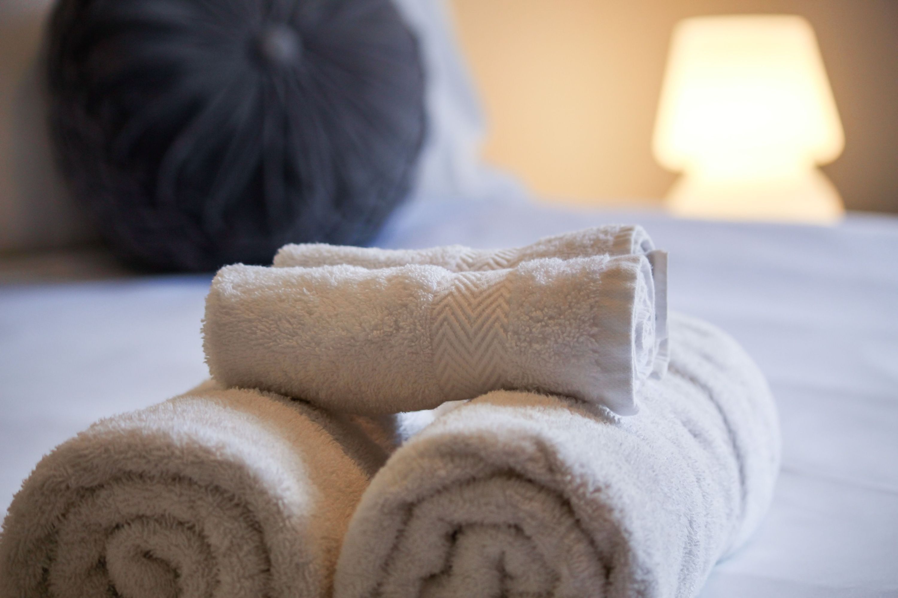 Neatly rolled towels stacked on a bed with a pillow in the background.