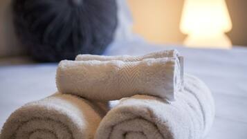 Neatly rolled towels stacked on a bed with a pillow in the background.