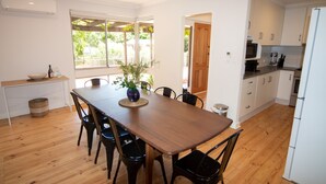 A modern kitchen with white cabinets, a wooden dining table, and a view of greenery outside. - Sandy Pool Shack - Pet Friendly (Seacliff Park)