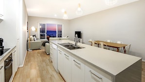 Een moderne keuken met een centraal eiland, een eethoek met een houten tafel en uitzicht op zee door een groot raam.