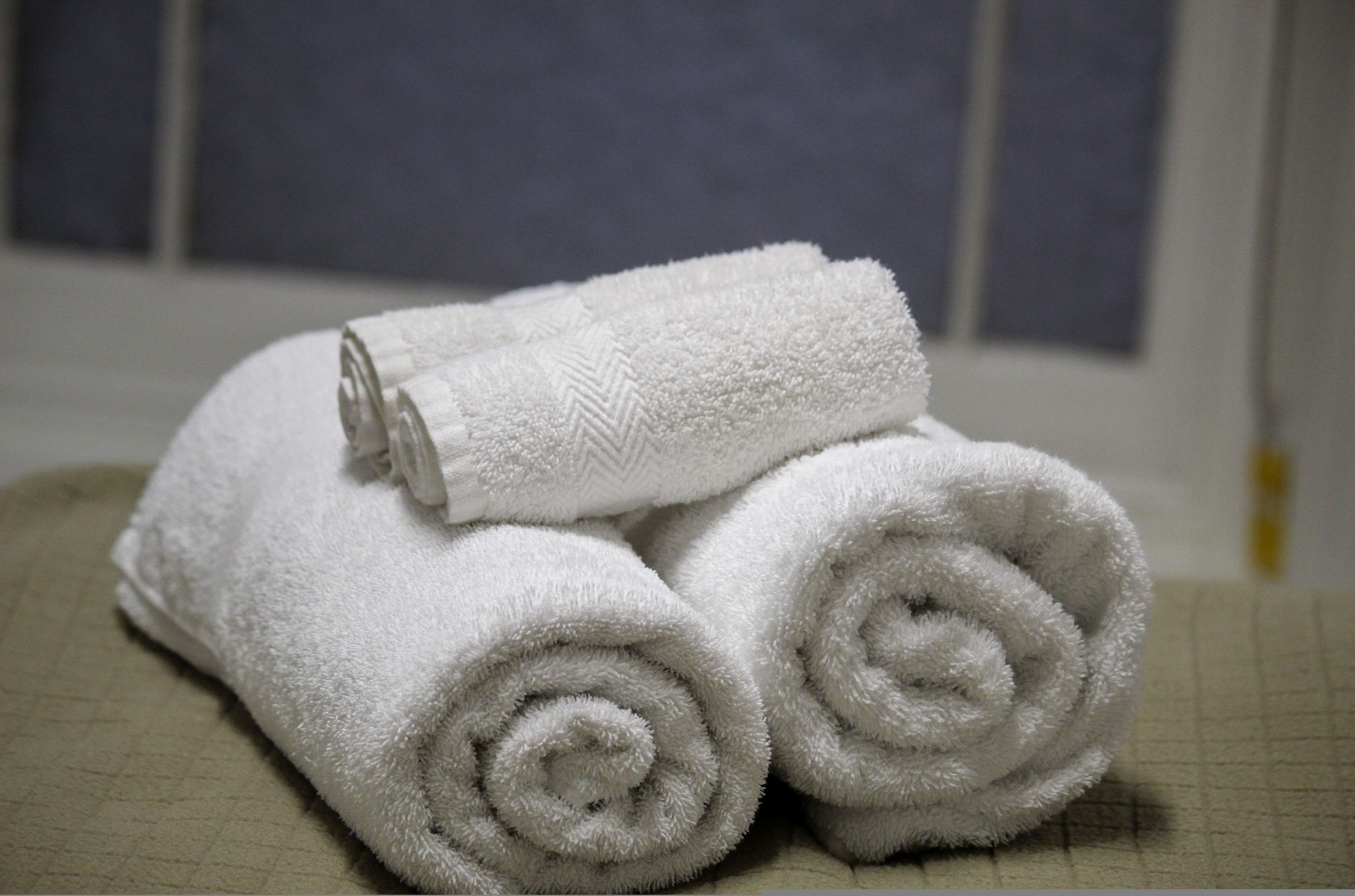 Three neatly rolled white towels stacked on a textured surface.
