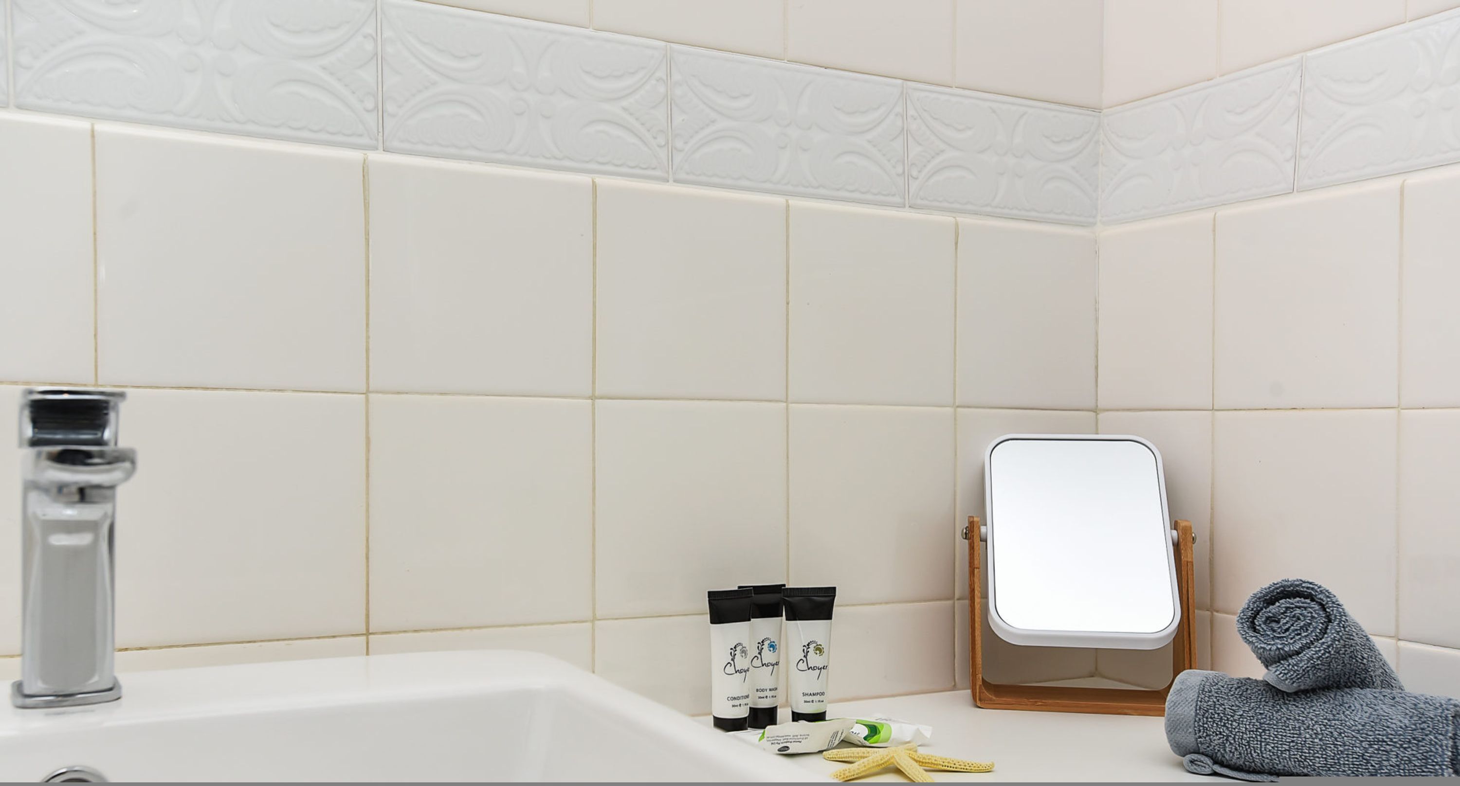 A bathroom with a sink, mirror, toiletries, and a towel.