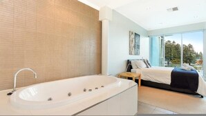 A modern bathroom with a large bathtub, a shower area, and a large window offering a view of trees. - Gallery Resort Style Penthouse no 13 (Victor Harbor)