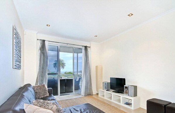 Un salon moderne avec un canapé, un téléviseur et un balcon offrant une vue sur la mer.