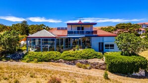 A modern two-story house with a red roof, large glass windows, and a balcony. - The Darling of Marina - A Hilltop and Sea Getaway (Wirrina Cove)