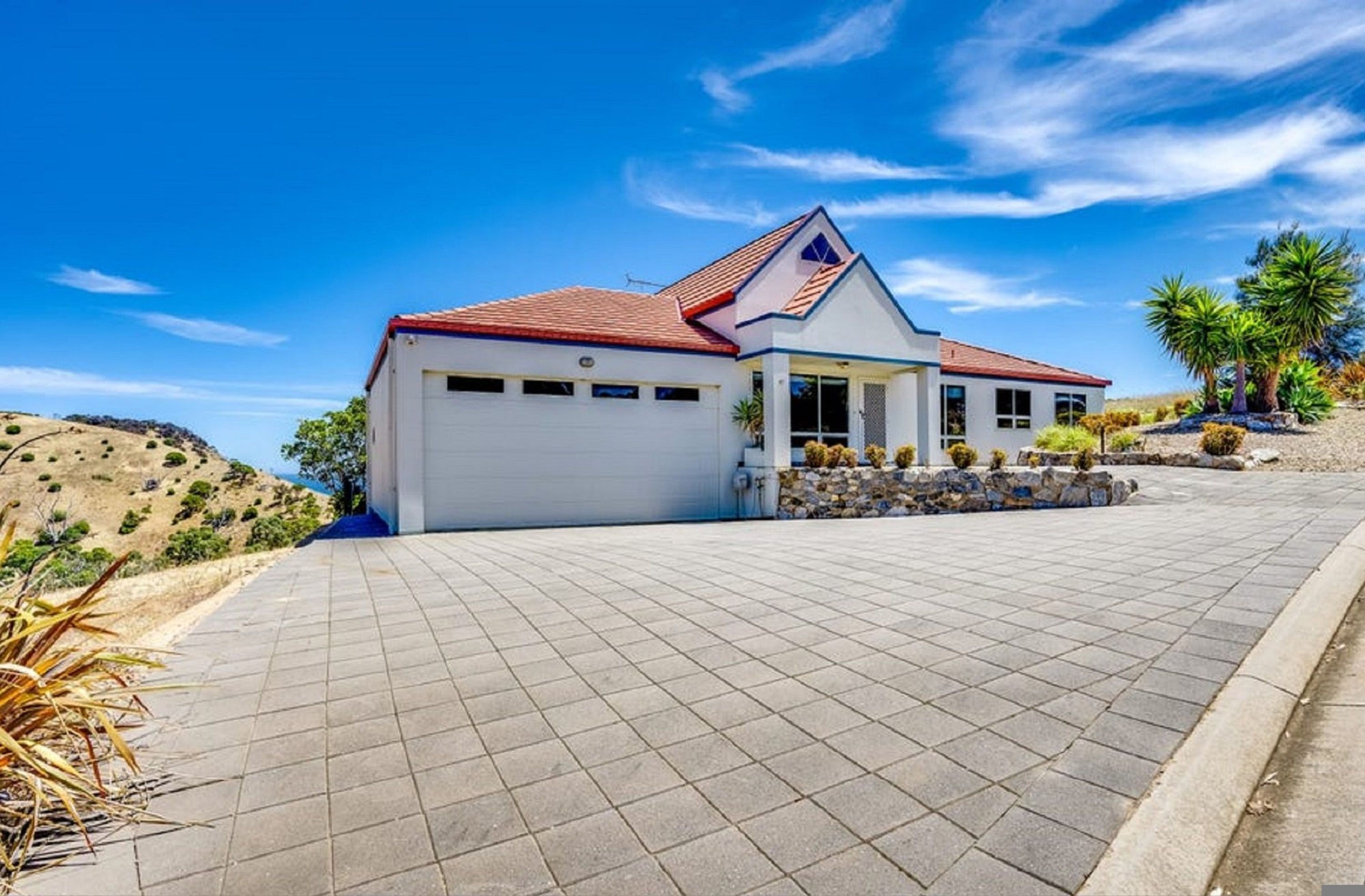 A single-story house with a red roof, a garage, and a paved driveway.