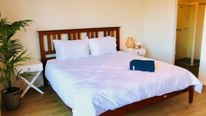 Una cama bien hecha con ropa de cama blanca, cabecera de madera y mesita de noche con lámpara.