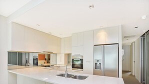 Une cuisine moderne avec des meubles blancs, des appareils en acier inoxydable et un îlot central doté d’un évier.