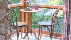 Une pièce d’angle avec une table en bois et deux chaises, une petite fenêtre donnant sur les arbres et un luminaire suspendu.