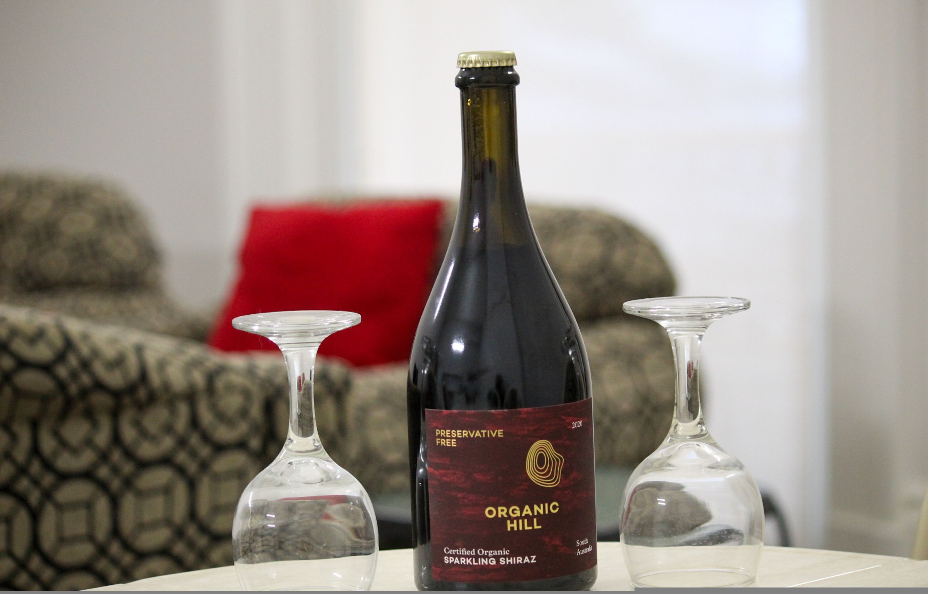 En flaska mousserande Shiraz-vin från Organic Hill står på ett bord tillsammans med två vinglas.