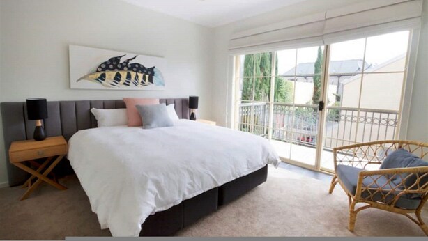 A bedroom with a large bed, a nightstand, a chair, and a balcony with a view.