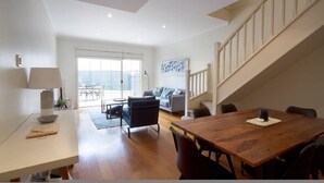A spacious living area with a wooden dining table, a sofa, and a staircase.