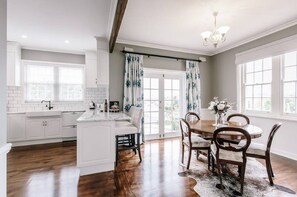 A modern kitchen with white cabinetry, a central island, and a dining area with a round table and chairs. - Byrne House - Modern-rustic Fireplace Wi-fi (Mount Gambier)