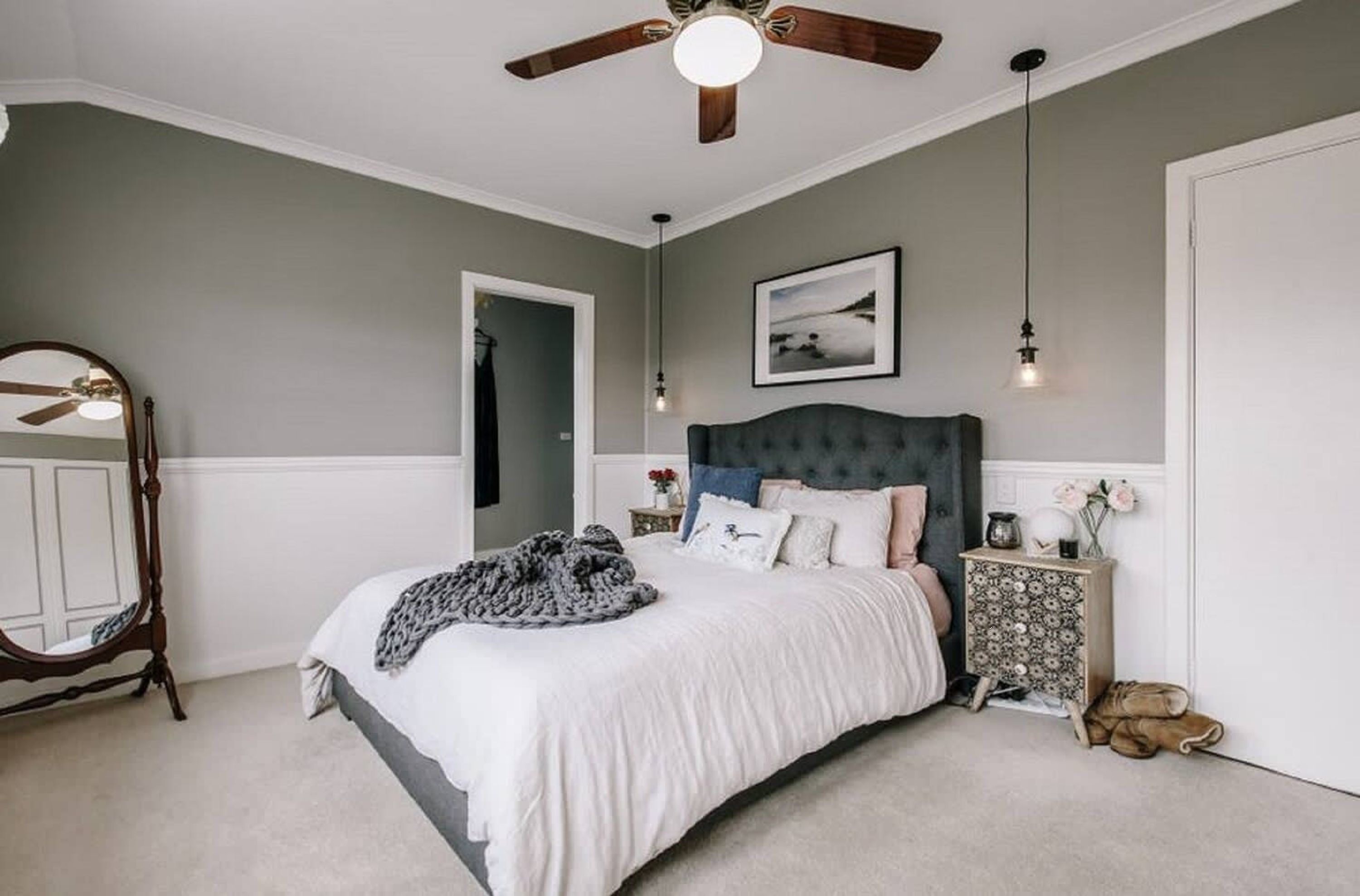 A bedroom with a large bed, a ceiling fan, a dresser, and a mirror.