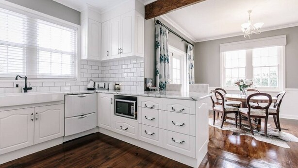 Een moderne keuken met witte kasten, een ingebouwde magnetron en een eethoek met een houten tafel en stoelen.