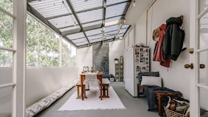 Een ruime kamer met een hoge plafond, een eethoek met een tafel en stoelen, een bank langs de muur en een wandkapstok.