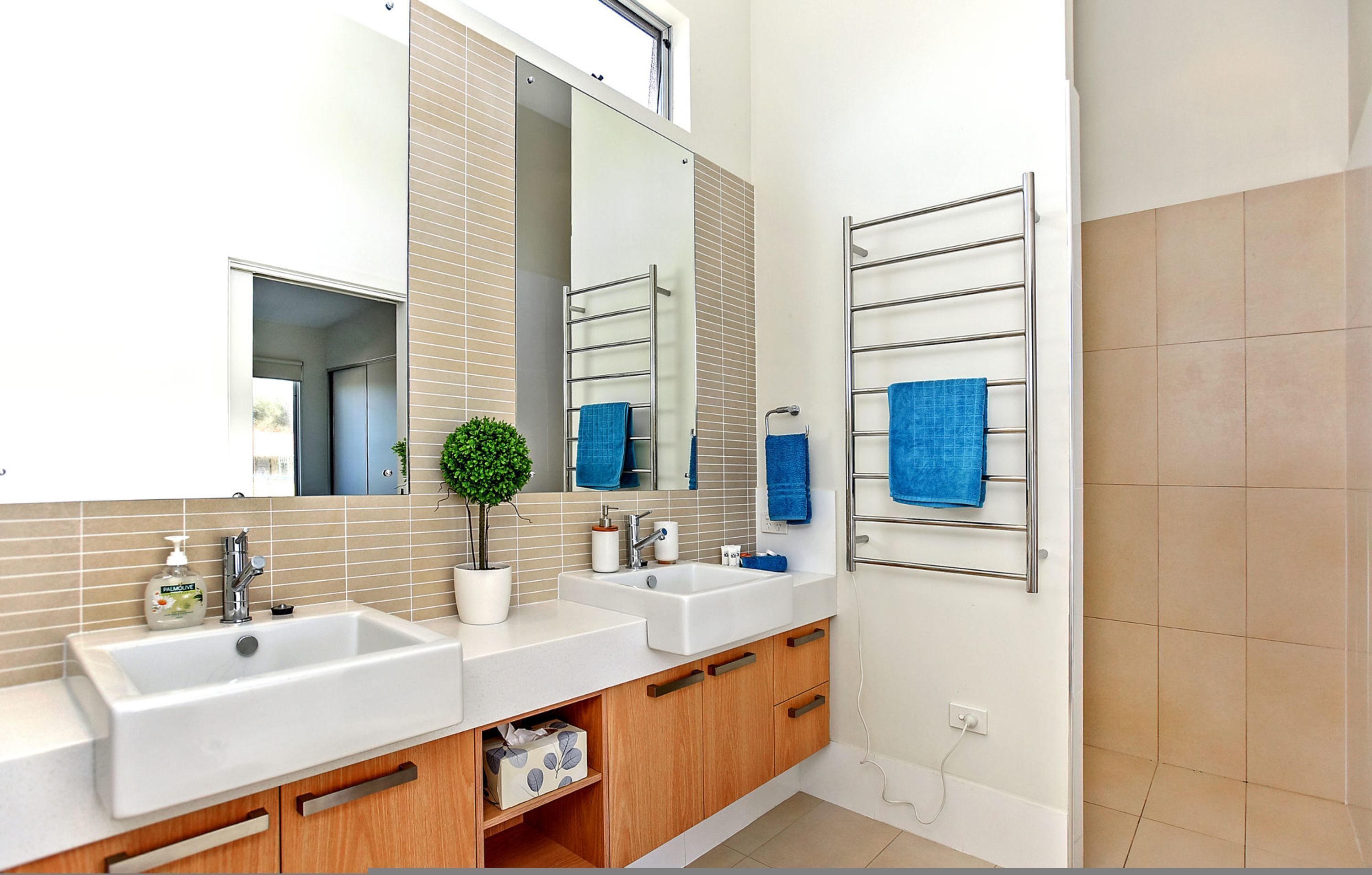 A modern bathroom with two sinks, a large mirror, and a towel rack.
