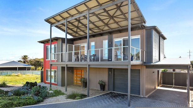 A modern two-story house with a covered balcony, a garage, and a landscaped garden.