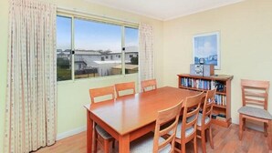 A dining area with a wooden table and chairs, a bookshelf, and a window with curtains. - Tahren Beachfront Shack Wifi - Pet-friendly (Middleton)