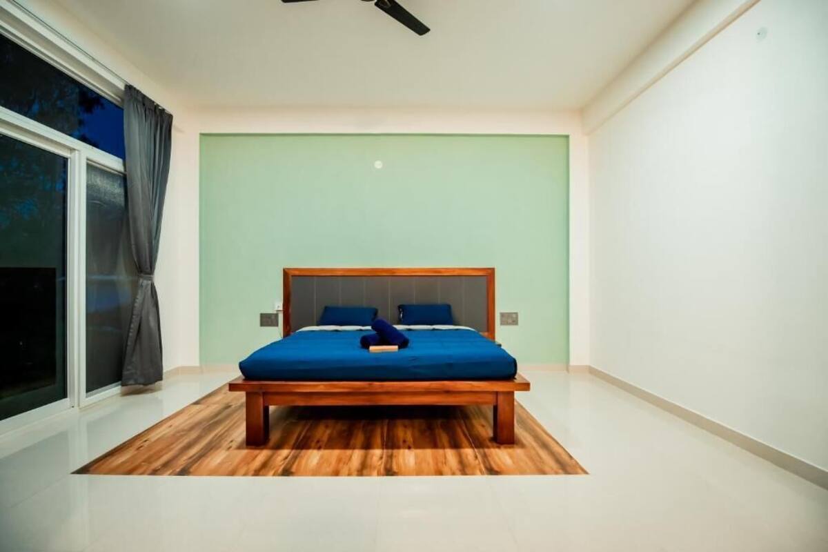 Una camera da letto con un letto di legno, una parete verde e un'ampia finestra con tende.
