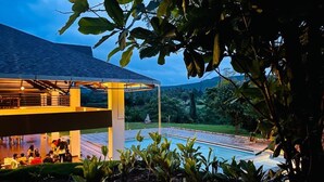 Un edificio moderno con zona de piscina, rodeado de exuberante vegetación y cielo despejado.