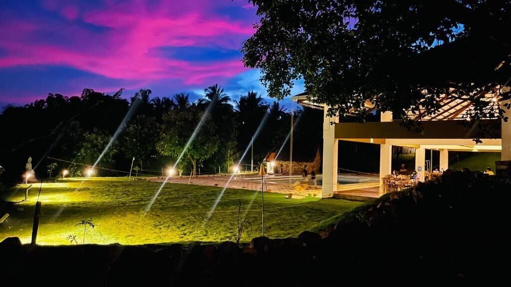 A modern building with a covered outdoor area and a well-lit lawn at dusk.