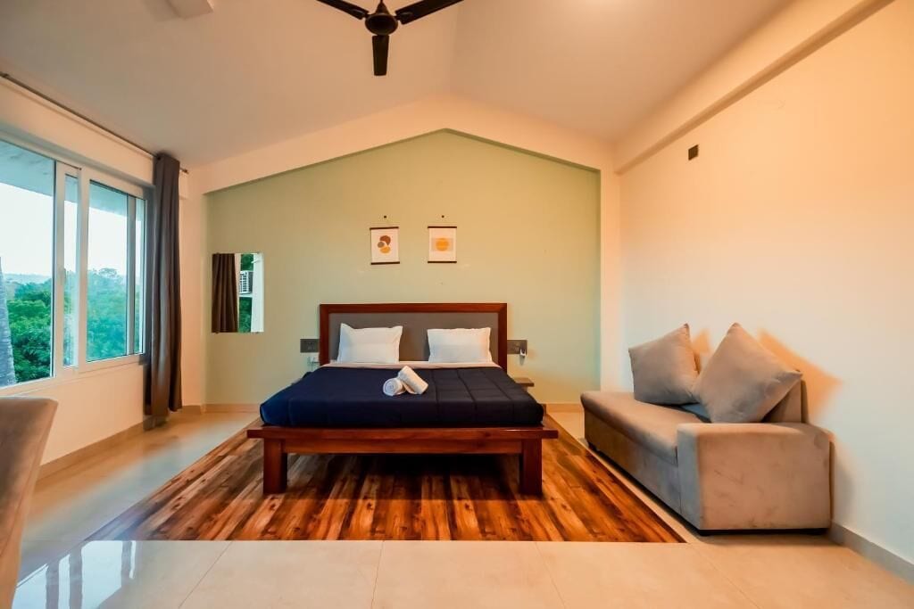 Un dormitorio con una cama de madera, un sofá gris y un ventanal con vistas a la vegetación.