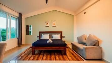 Un dormitorio con una cama de madera, un sofá gris y un ventanal con vistas a la vegetación.
