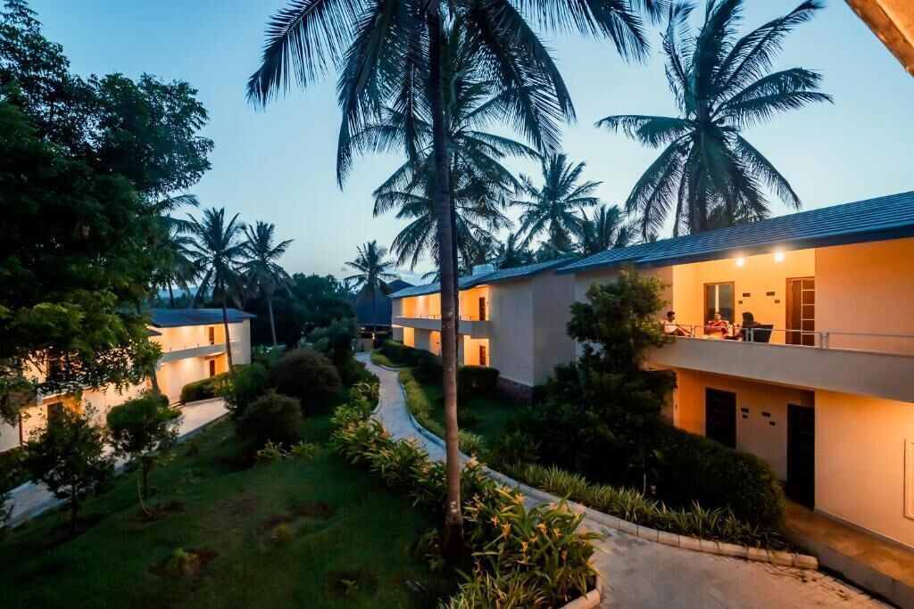 Un resort con varias edificaciones de dos pisos, un jardín cuidado y palmeras.