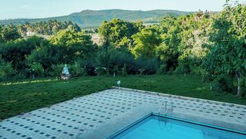 A swimming pool with a tiled deck and a view of a lush green landscape with trees and hills in the background.