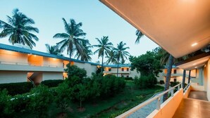 Un patio de hotel con un paseo cubierto, palmeras y un jardín cuidado.