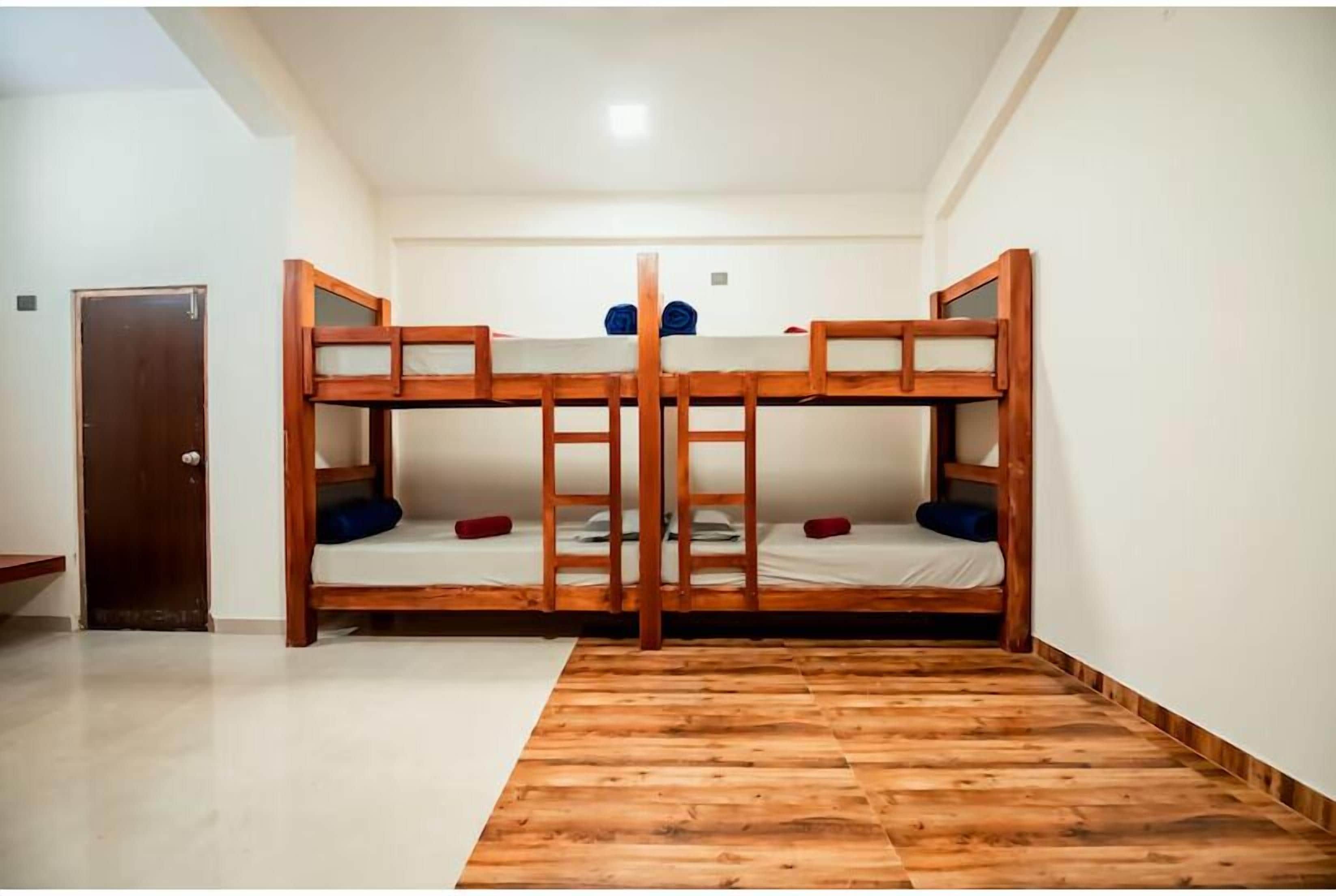 A room with four bunk beds arranged in a square, wooden floor with a white door on the left.