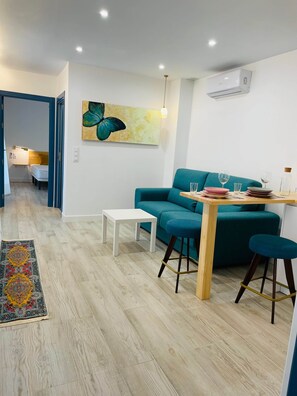 A modern living room with a teal sofa, a wooden dining table, and a white coffee table. There is a painting on the wall and an air conditioning unit mounted on the wall. - Apartamento Bravo Murillo con garaje (Badajoz)