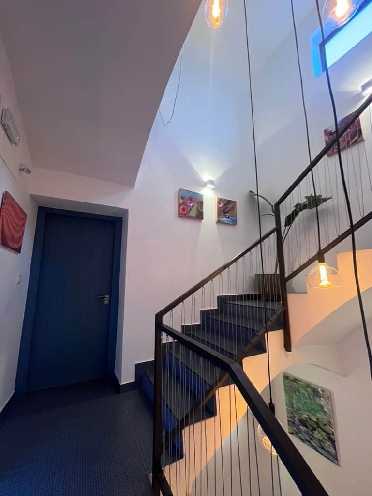 A staircase with a black railing, a blue door, and wall-mounted artwork.