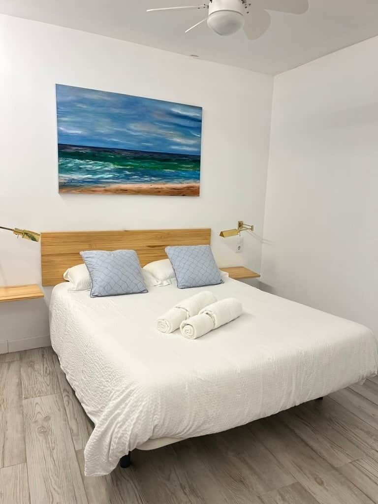Een net opgemaakt bed met een witte dekbedovertrek, twee kussens en opgerolde handdoeken.