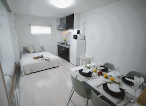 Cozy apartment with a neatly made bed, compact kitchenette, and dining area.